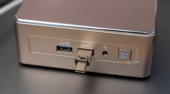A small Geekom mini PC with a USB-C flash drive plugged into the front panel.
