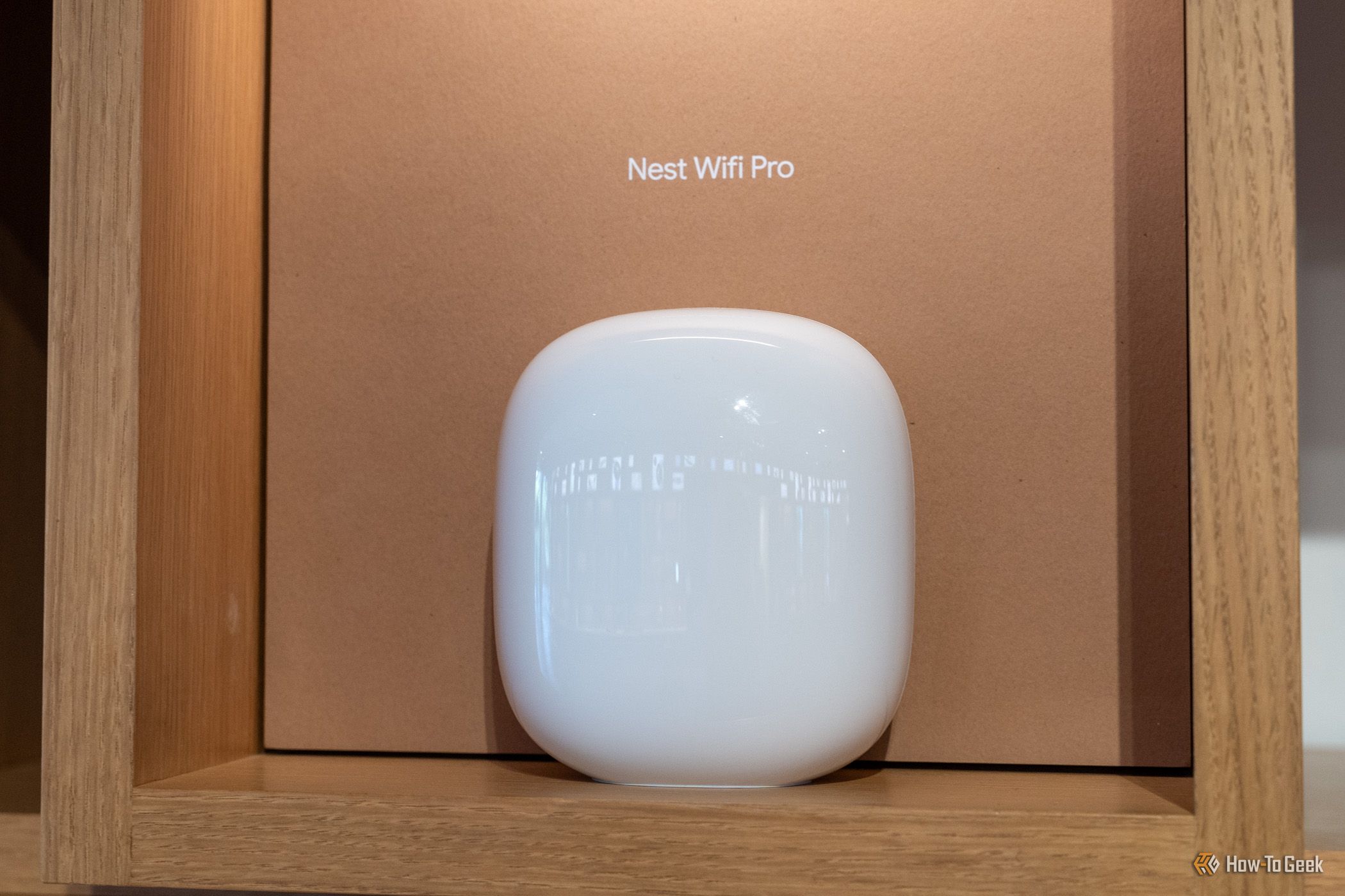 A white Nest Wifi Pro router displayed on a wooden shelf.