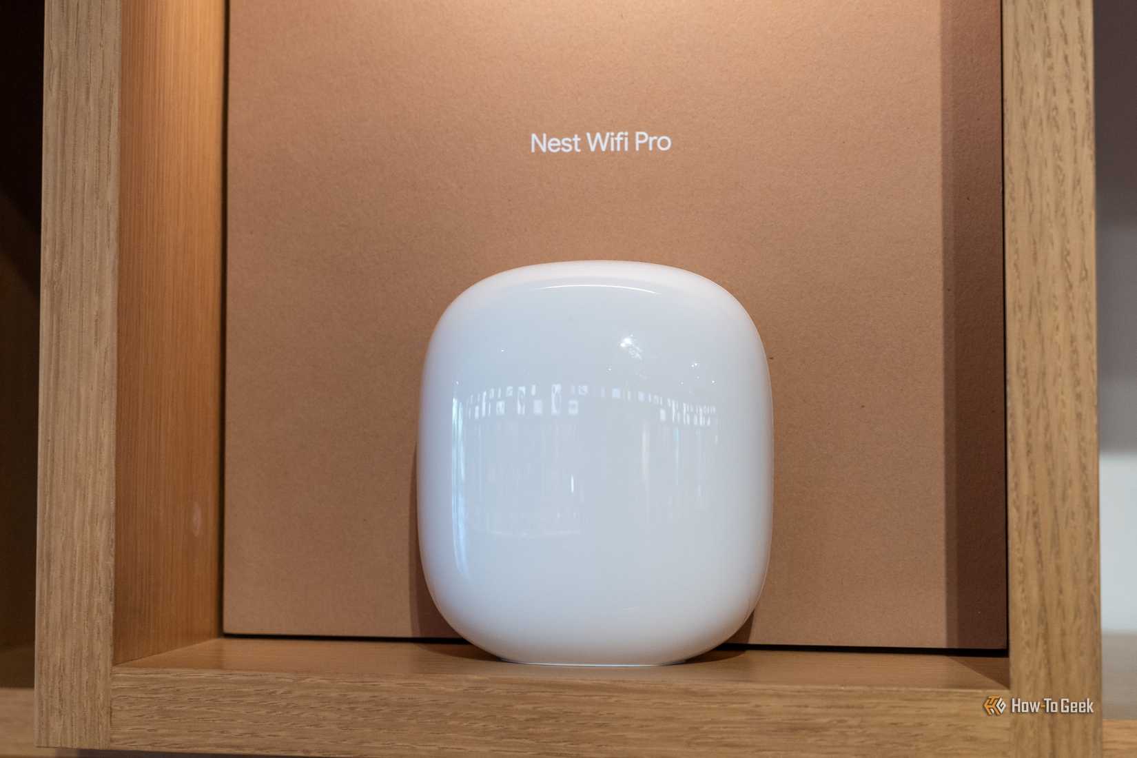 A white Nest Wifi Pro router displayed on a wooden shelf.
