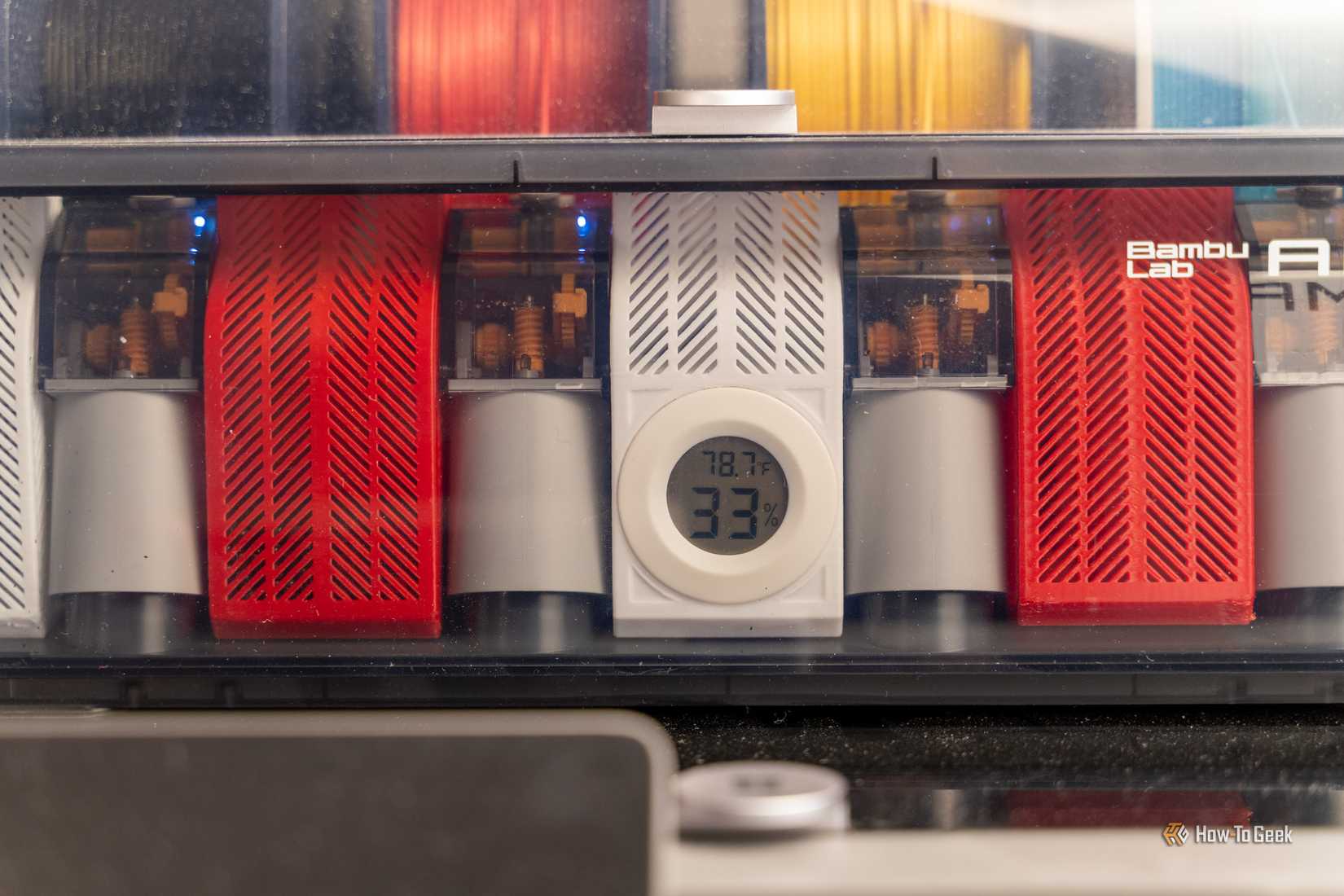 The Bambu Lab AMS unit with filament and desiccant in it showing a hygrometer for humidity and moisture percentage.