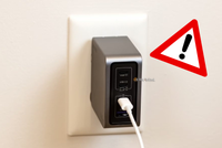 The Ugreen Nexode Pro 160 USB-C Wall Charger plugged into an outlet with a warning symbol next to it.