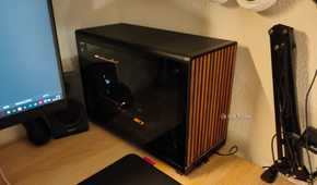 An ITX PC tower stands on a desk with warm light shining on it.