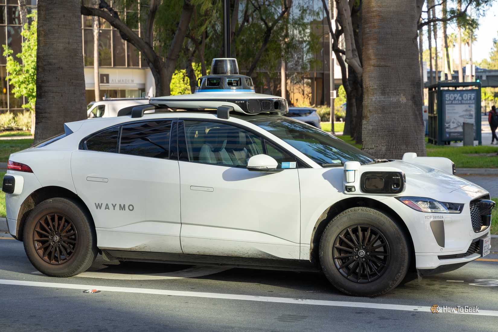 Side view of a Waymo self-driving Jaguar I-PACE SUV stopped on a city street.