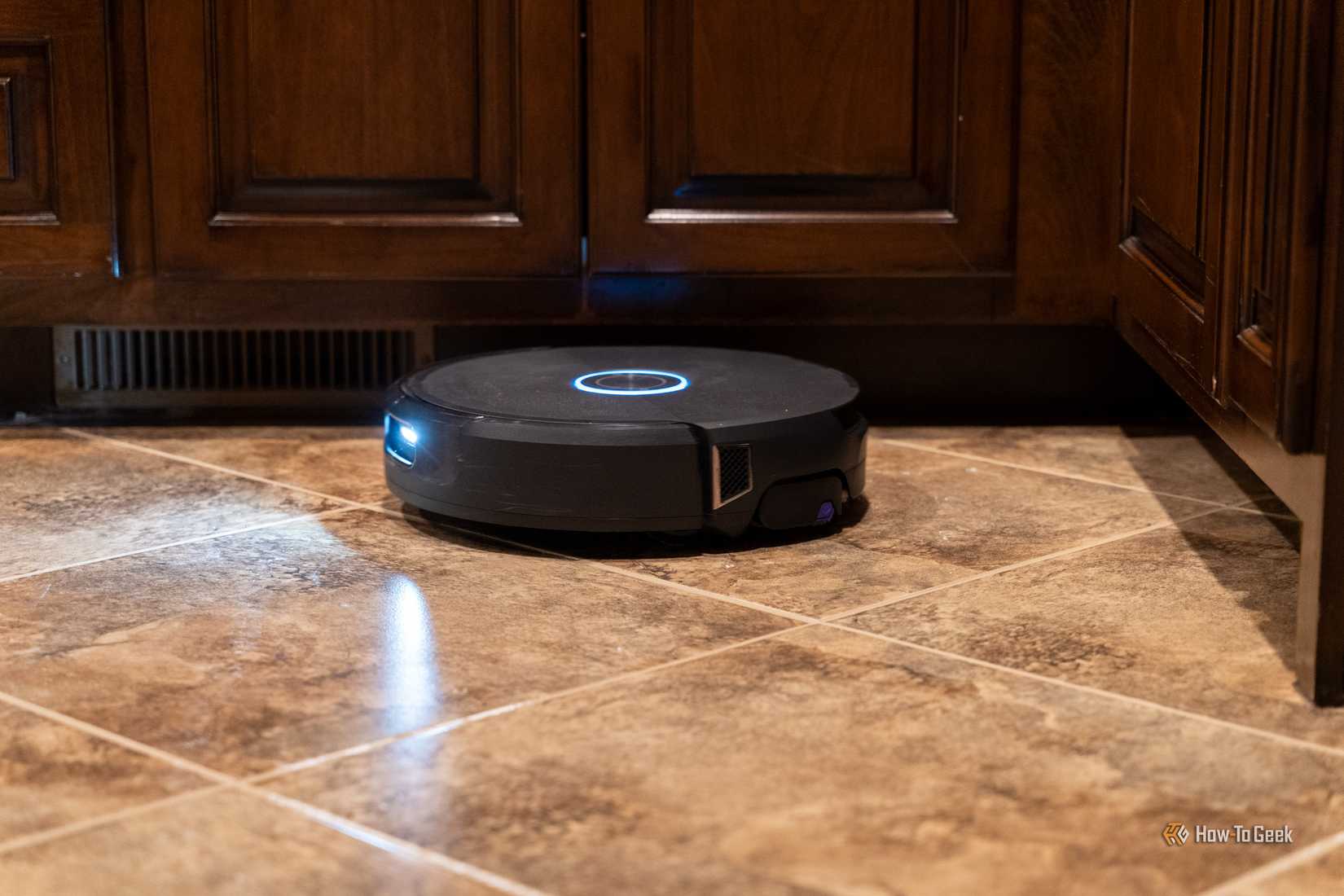 Low side view of the Narwal Flow 2 robot vacuum cleaning under kitchen cabinets.