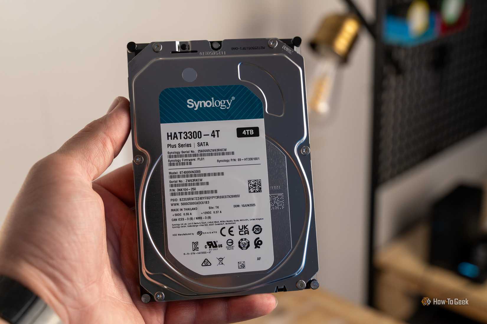 Synology HAT3300-4T 4TB hard drive held in front of the DS225 Plus NAS.