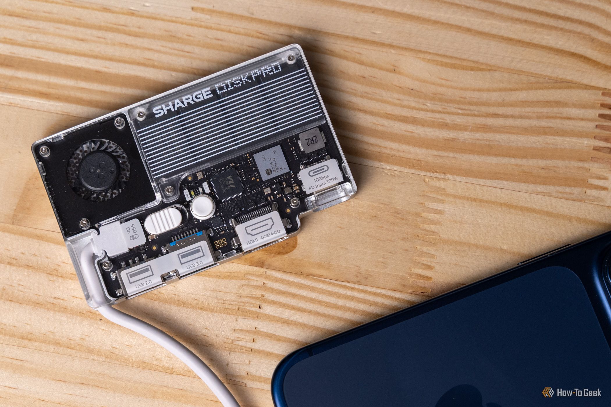 The transparent Sharge Disk Pro connected to the back of an iPhone 17 Pro on a wooden table.