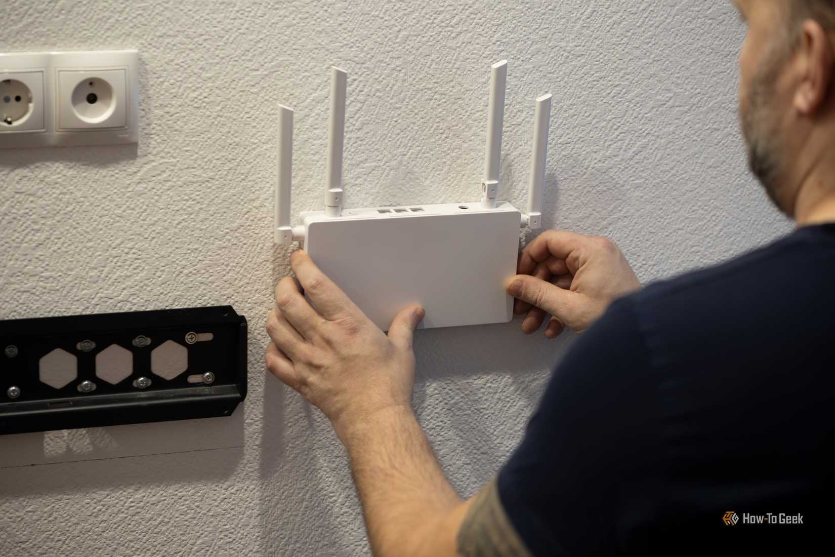 A man mounting a white Wi-Fi router on a white wall next to a TV mount.