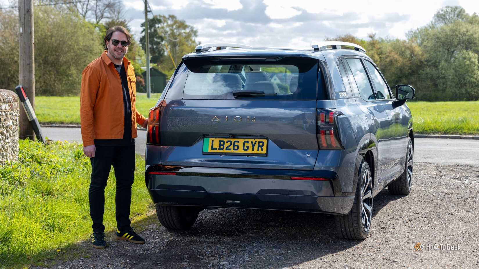 Static rear 3/4 shot of a gray AION V with a man stood beside it.