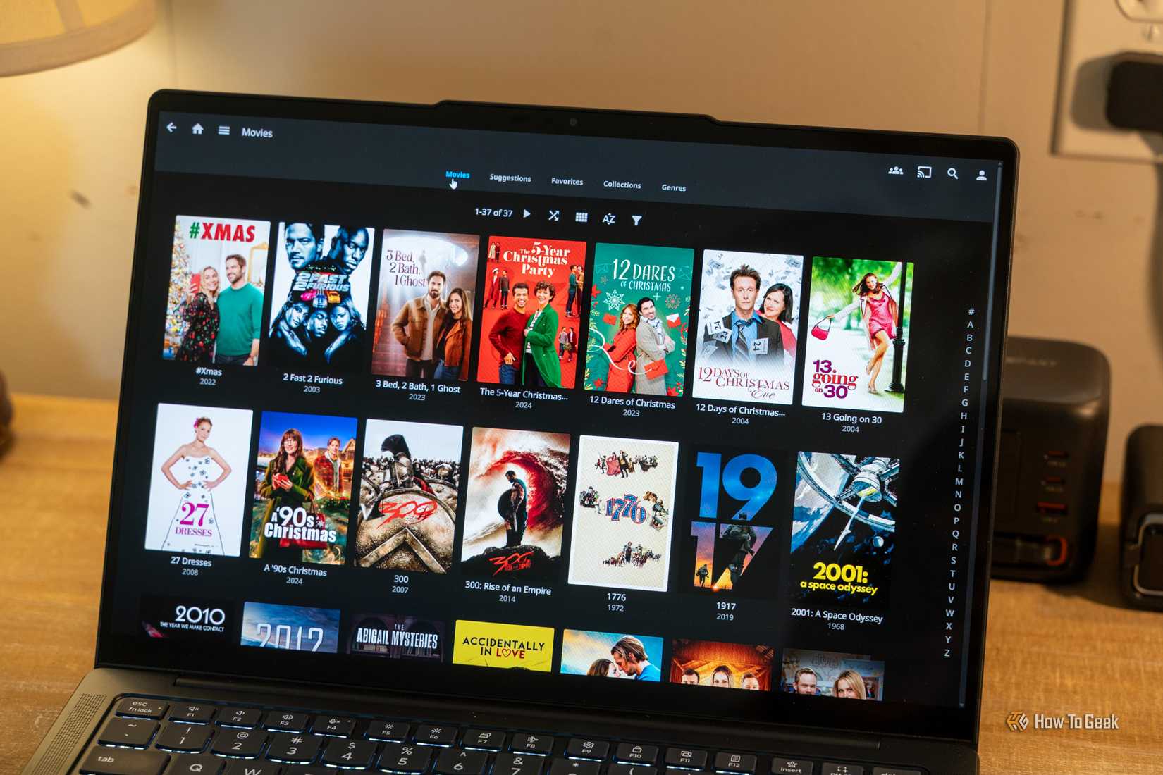 Laptop showing Jellyfin Movies library grid with alphabetical sidebar.