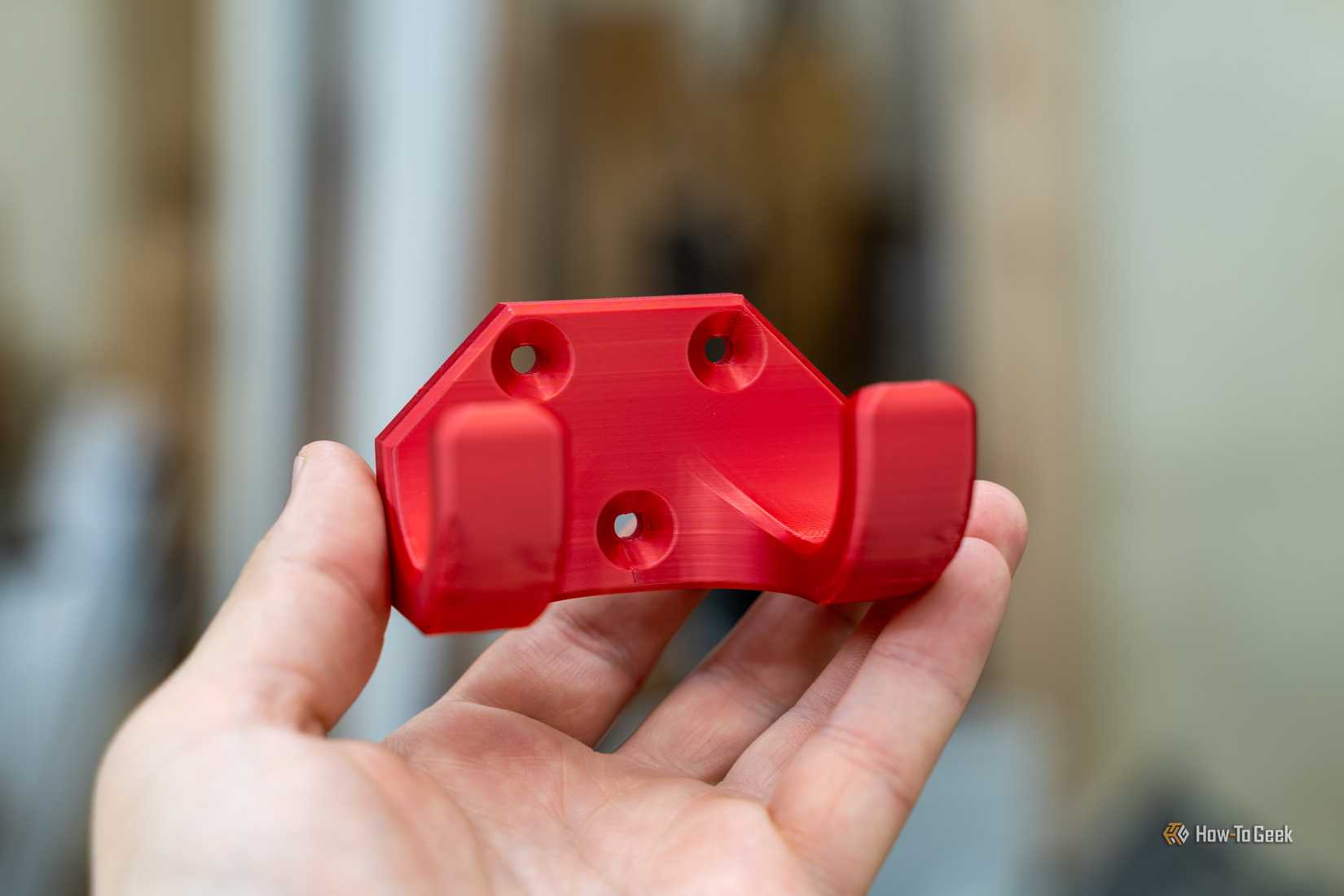 Red 3D printed wall hook for shop organization held in hand.