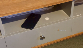 An NFC tag stuck to the shelf of a coffee table with an iPhone lying next to it.