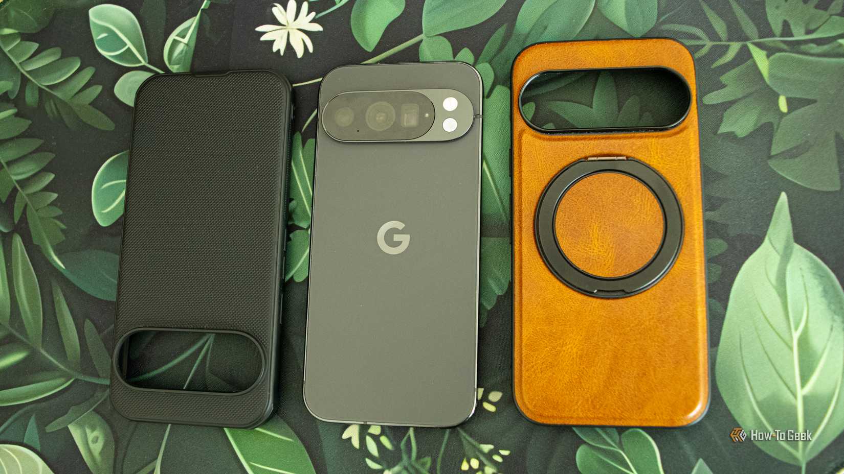 A Google Pixel 10 Pro lying on a desk mat with two phone cases surrounding it. 