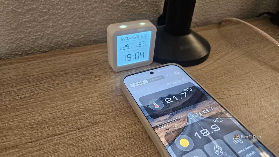 Un téléphone affichant une température intérieure de 21,7 degrés Celsius à côté d'un thermostat affichant 25,3 degrés Celsius.