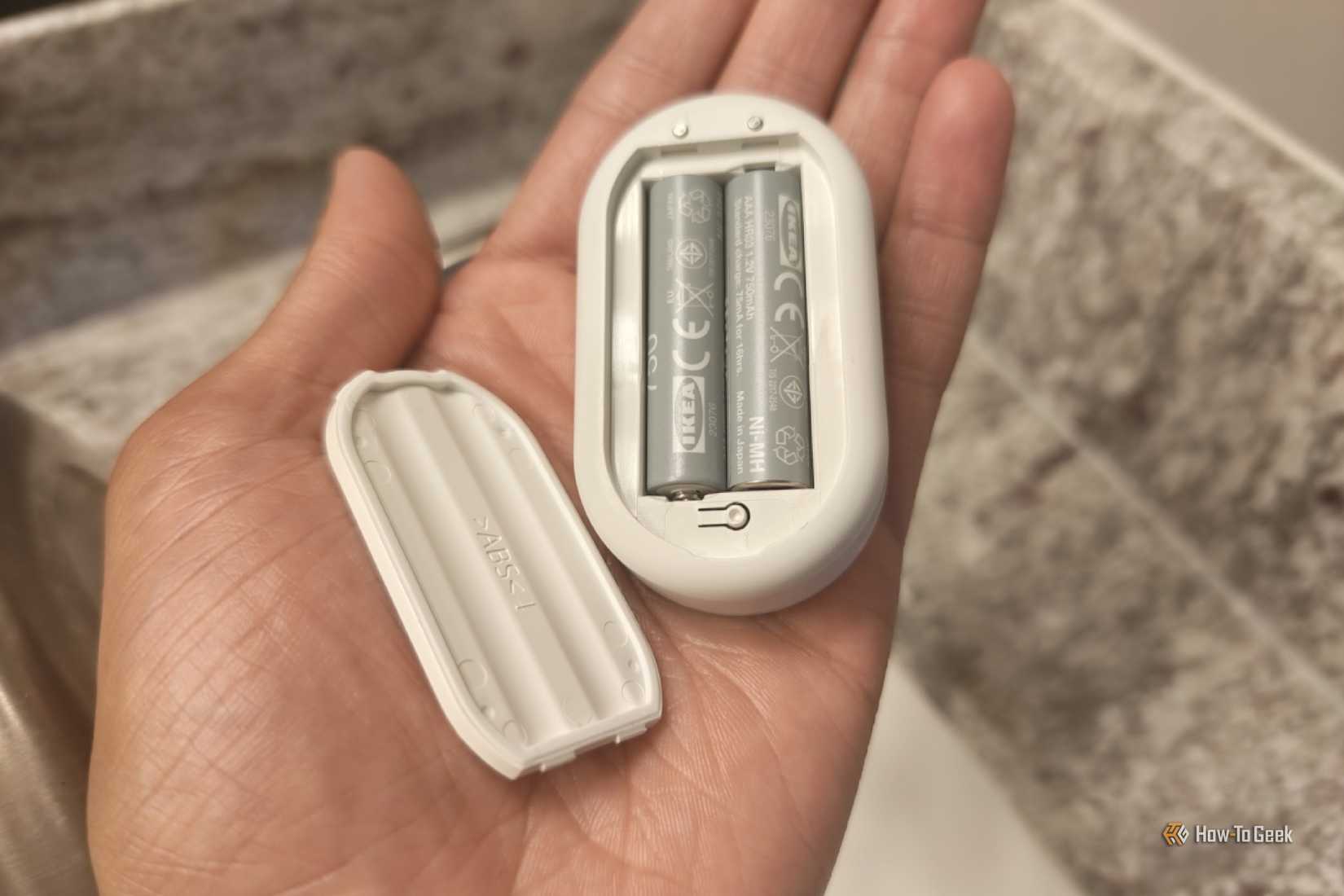 Hand holding an IKEA KLIPPBOK water leak sensor with the batteries visible.