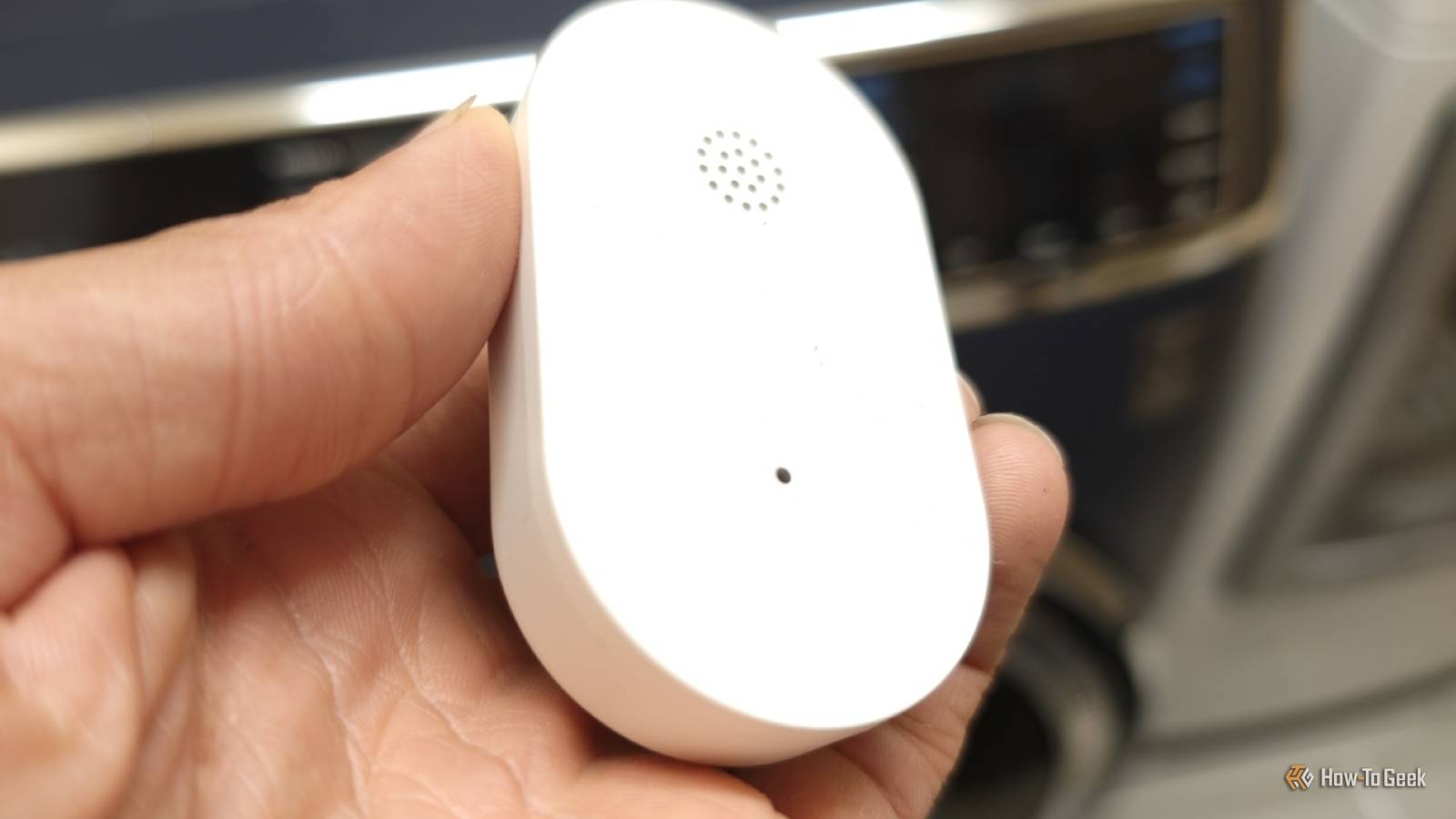 Hand holding an IKEA KLIPPBOK water leak sensor in front of a washer and dryer.