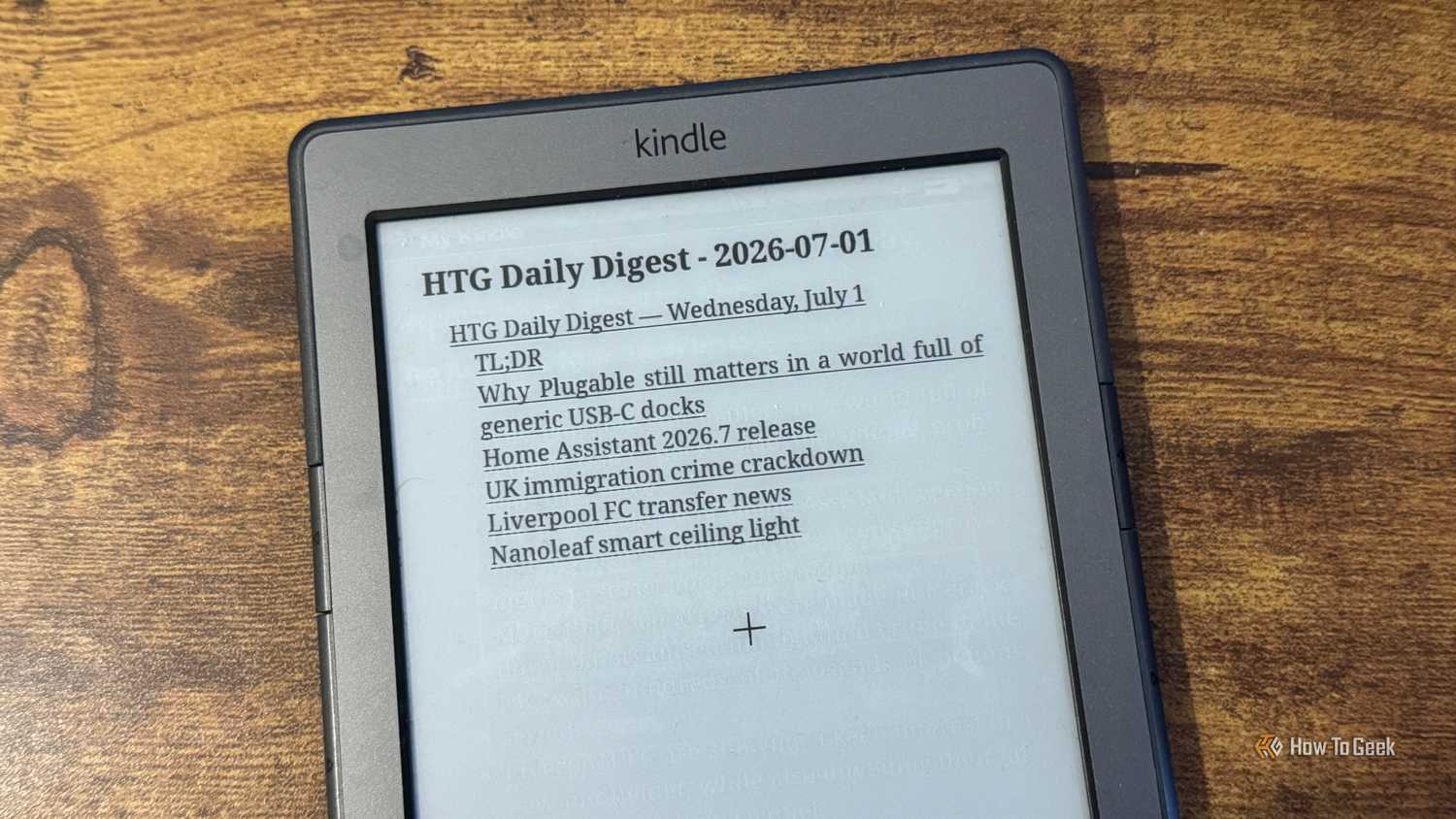 A Kindle 4 tilted on a desk showing the HTG Daily Digest for July 1 2026 title page with a bulleted headline list.