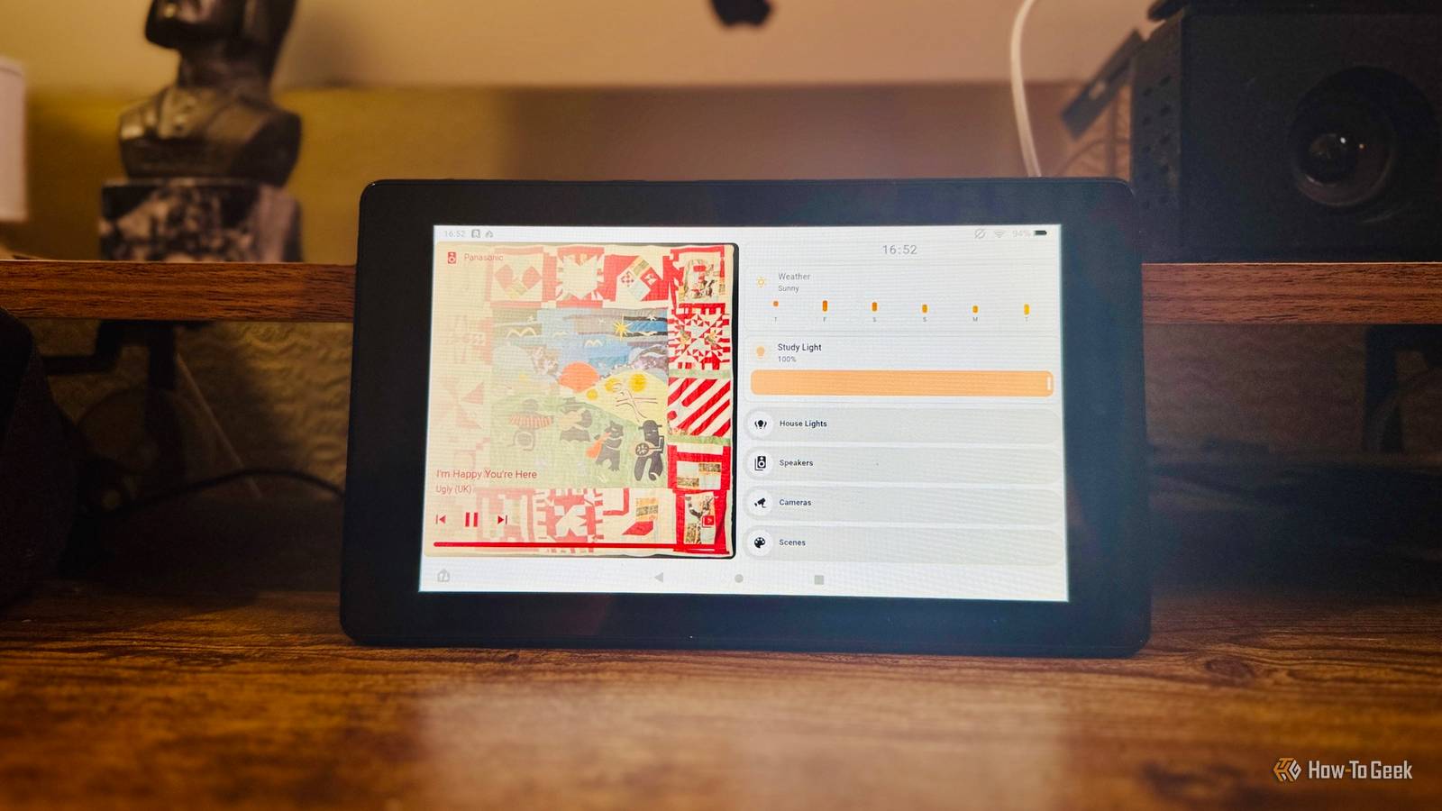 A tablet leaning on a shelf between a figurine and a smart speaker showing a Home Assistant dashboard.