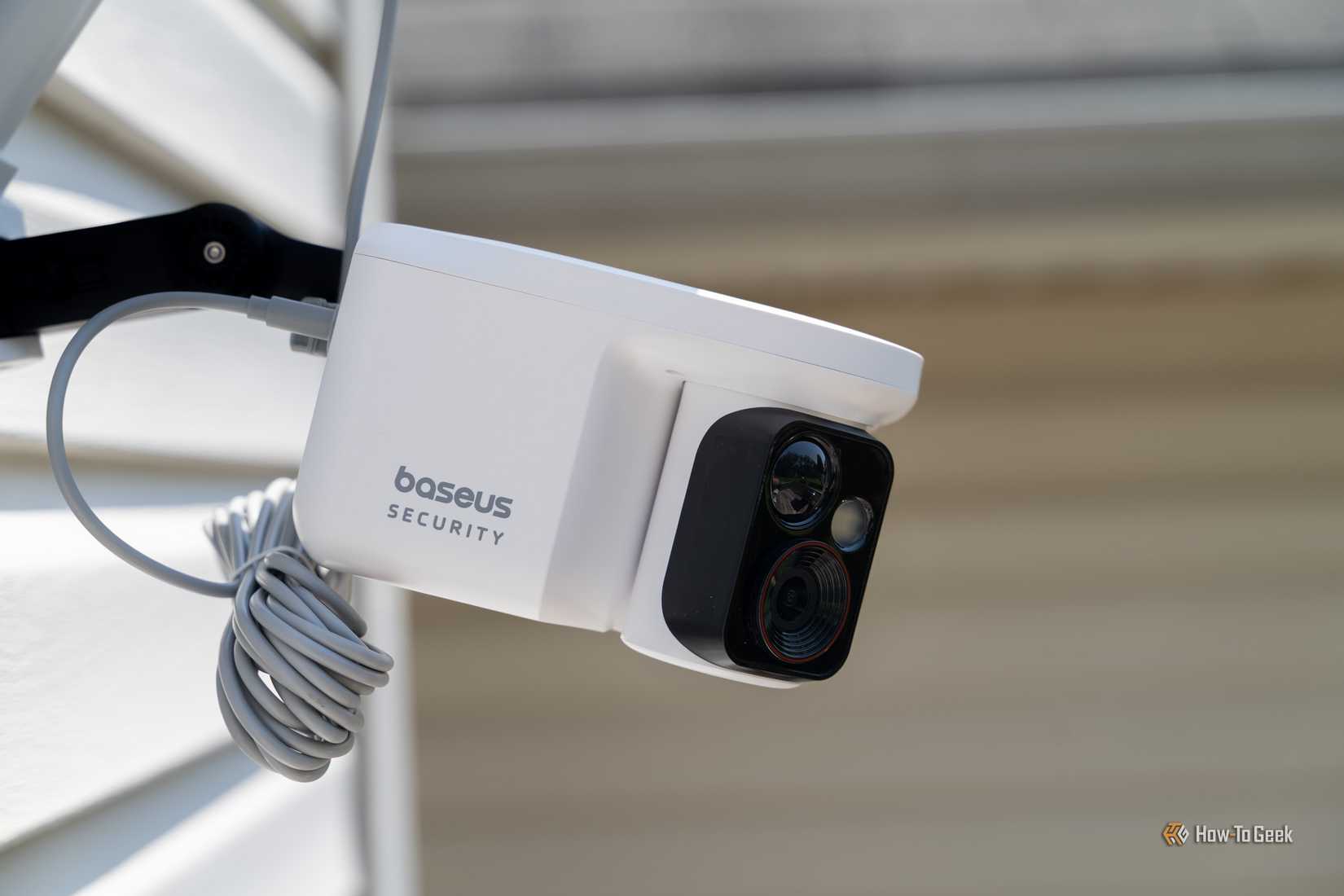 Baseus Security X1 Pro close-up of front camera head with coiled cable on wall mount.