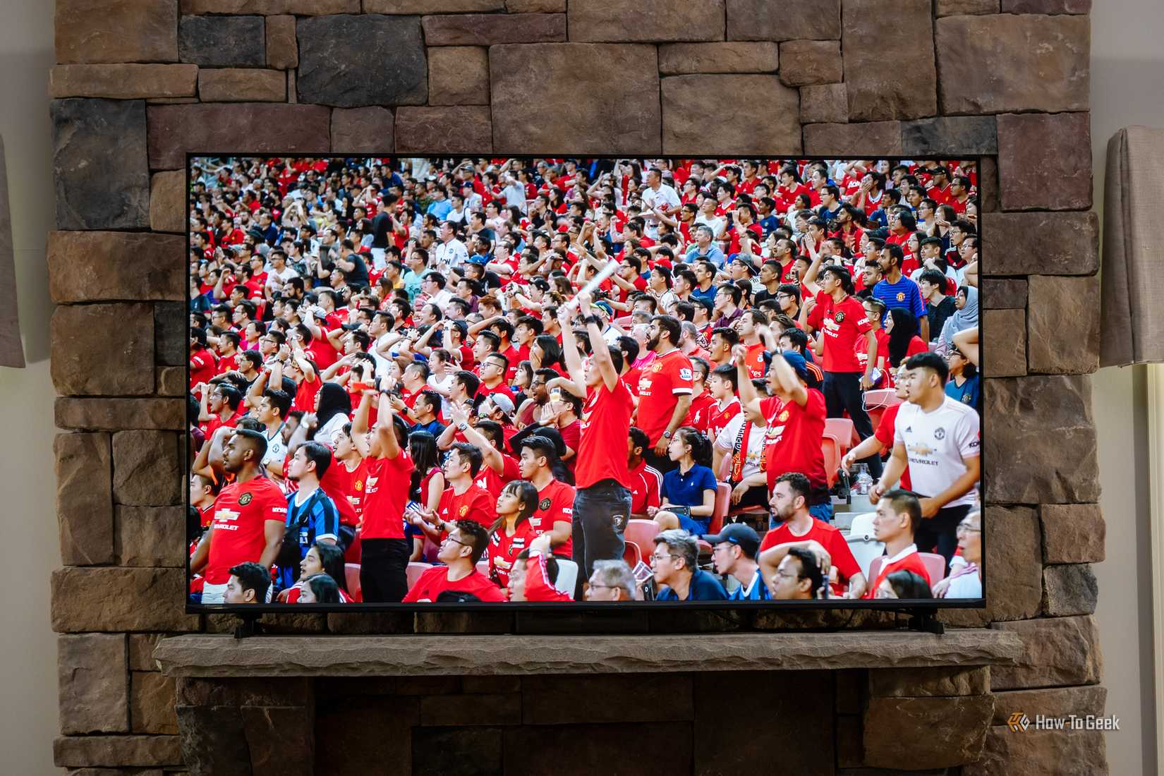 Hisense U6 Pro TV mounted on stone fireplace displaying close-up of soccer fans in red jerseys cheering in a stadium.