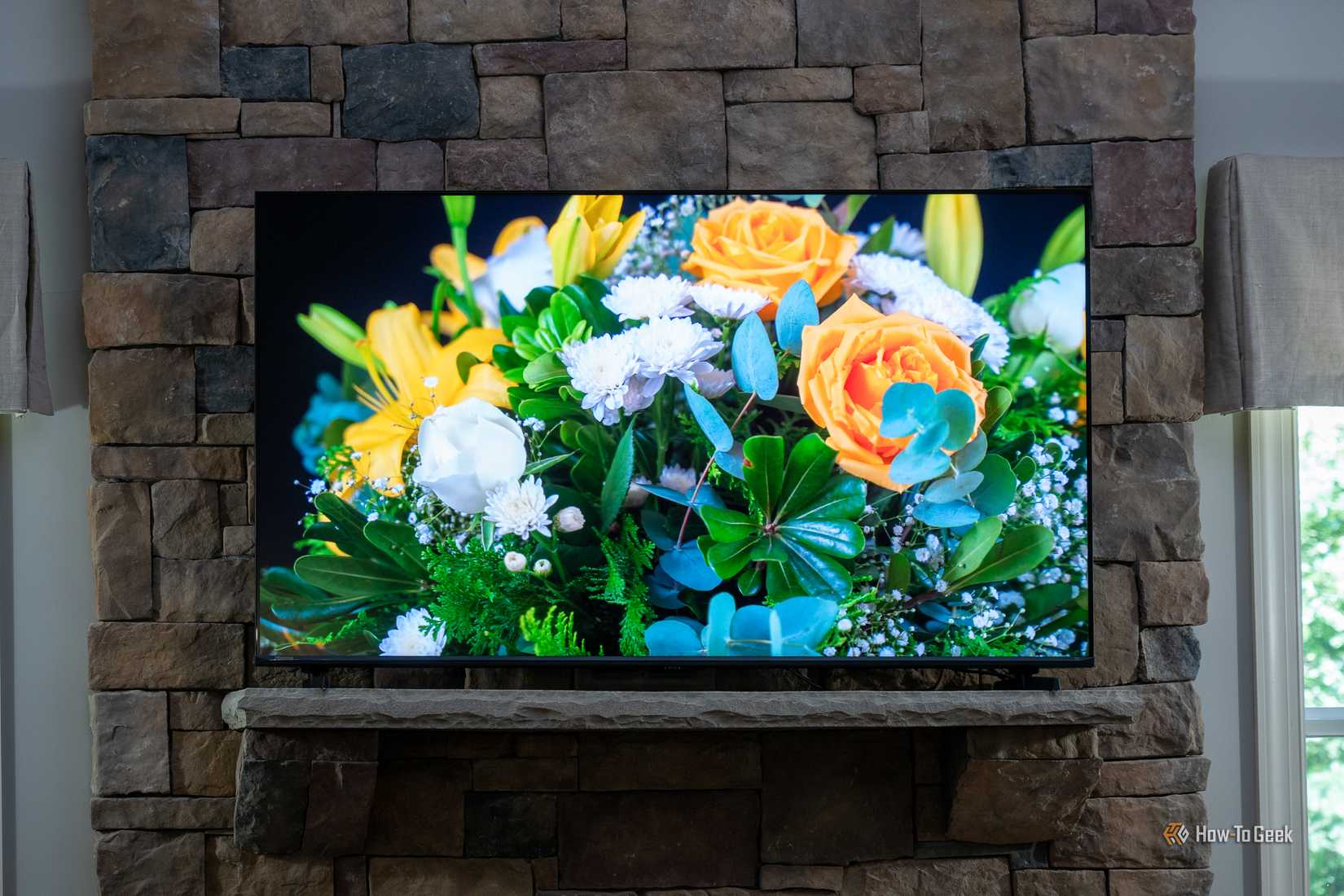 Hisense U6SF Pro TV mounted on stone fireplace displaying colorful floral bouquet with orange roses and yellow lilies.