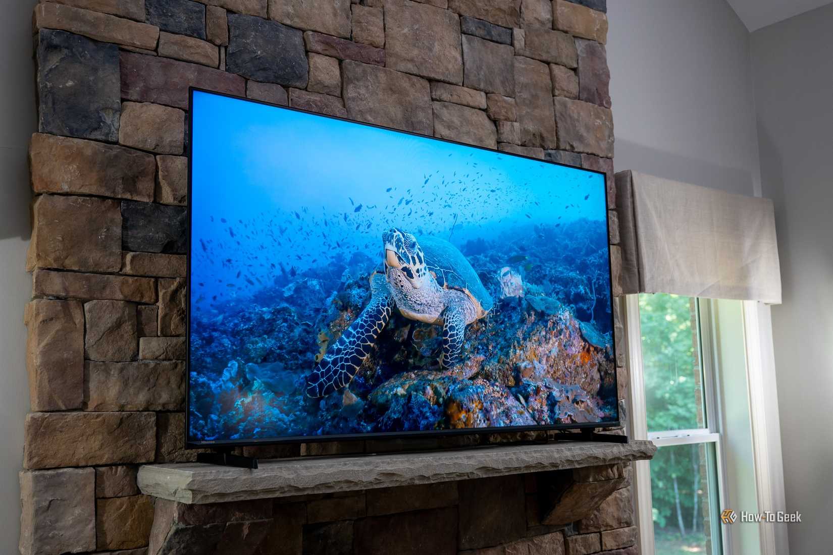 Hisense U6SF Pro TV mounted on stone fireplace displaying sea turtle swimming over colorful coral reef.