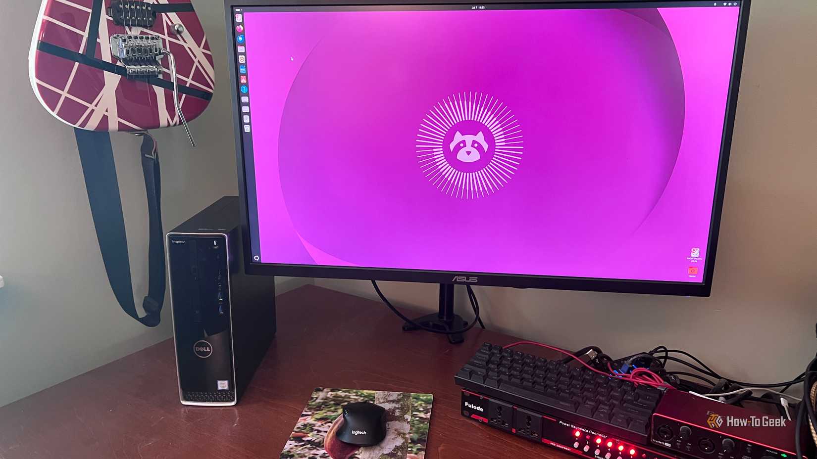 AN image of a computer running Ubuntu Linuxsitting on a desktop with a keyboard and a mouse. On the left there is a guitar hanging on the wall.