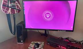 AN image of a computer running Ubuntu Linuxsitting on a desktop with a keyboard and a mouse. On the left there is a guitar hanging on the wall.