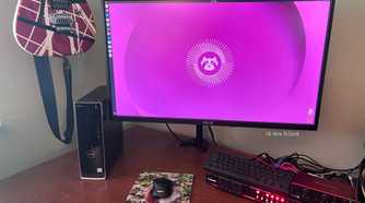AN image of a computer running Ubuntu Linuxsitting on a desktop with a keyboard and a mouse. On the left there is a guitar hanging on the wall.