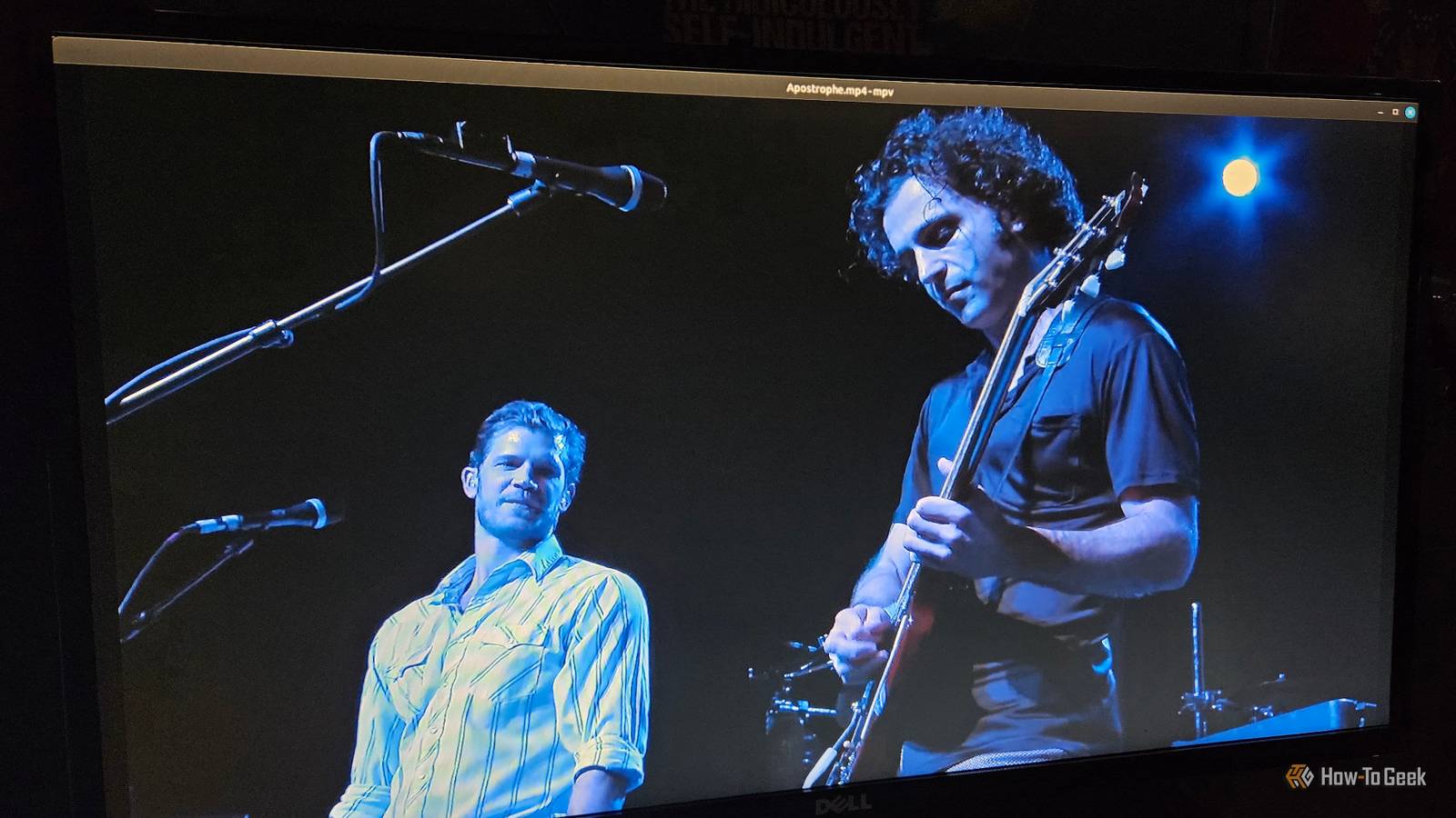 A video playing on a monitor of two musicians performing on stage.
