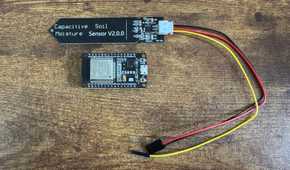 Capacitive soil moisture sensor and ESP32 development board connected by wires laid separately on a wooden table with the sensor above the ESP32.