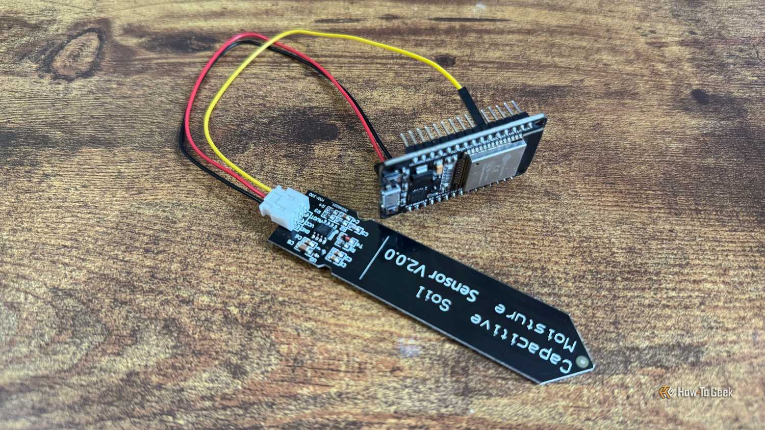Capacitive soil moisture sensor and ESP32 development board mounted in a black pin header bracket photographed upside down.