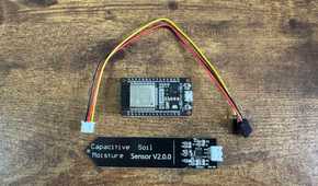 ESP32 development board and capacitive soil moisture sensor connected by wires laid separately on a wooden table with the ESP32 above the sensor.