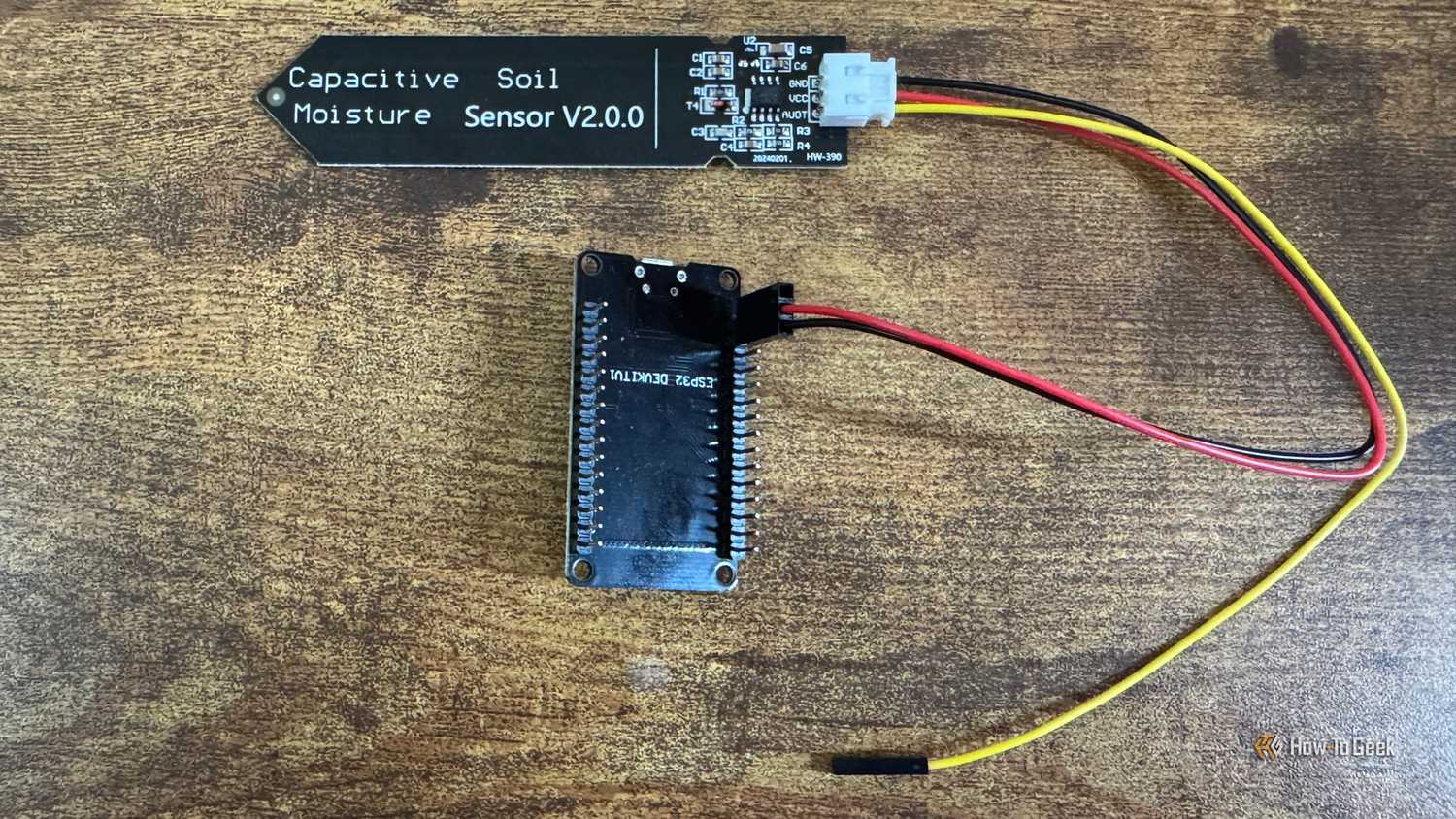 ESP32 development board mounted in a black pin header bracket connected to a capacitive soil moisture sensor by wires.
