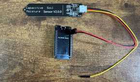 ESP32 development board mounted in a black pin header bracket connected to a capacitive soil moisture sensor by wires.