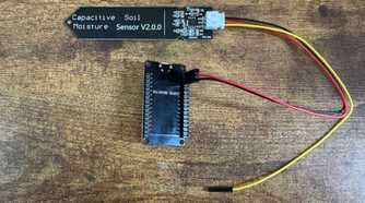 ESP32 development board mounted in a black pin header bracket connected to a capacitive soil moisture sensor by wires.