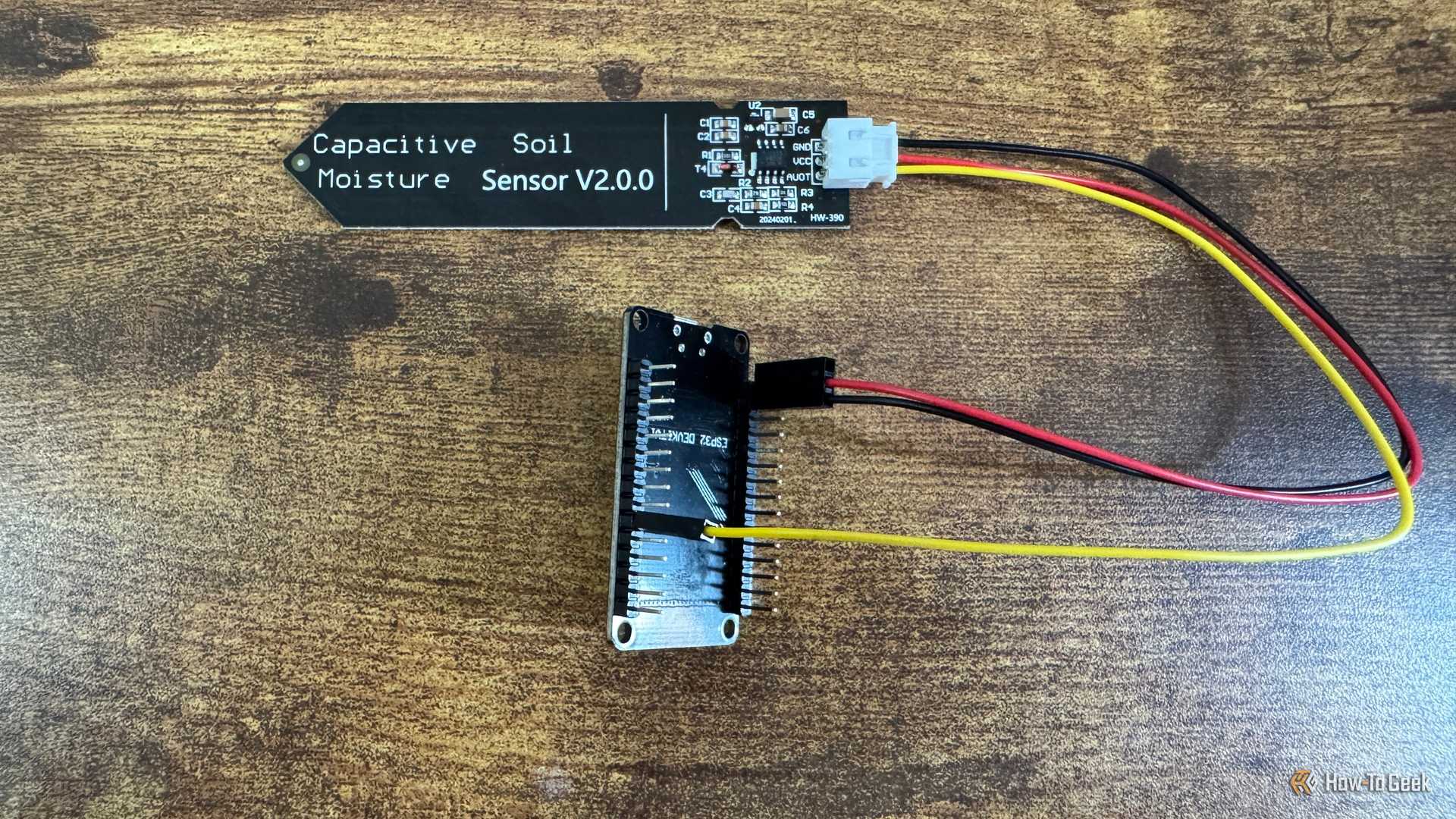 ESP32 development board mounted in a black pin header bracket seen from a higher angle connected to a capacitive soil moisture sensor.