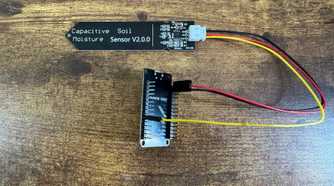 ESP32 development board mounted in a black pin header bracket seen from a higher angle connected to a capacitive soil moisture sensor.