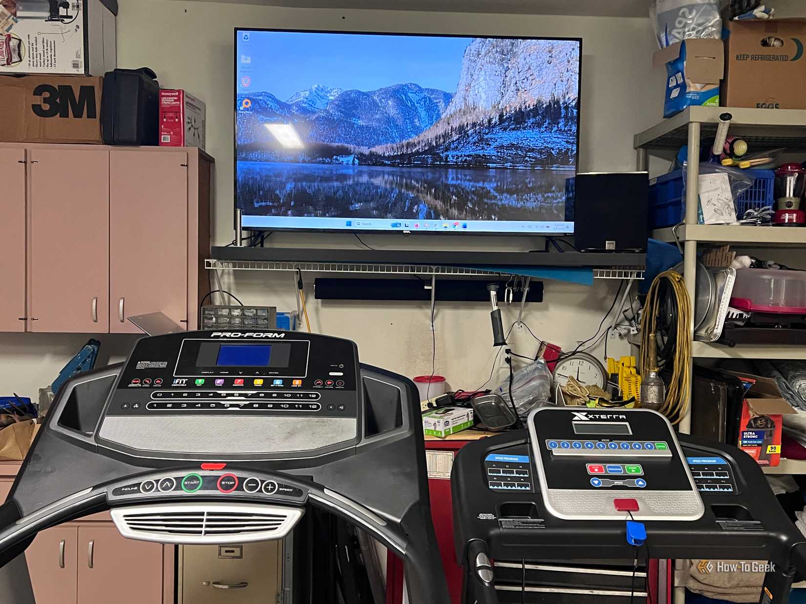 An image of a giant monitor in front of two treadmills in a garage.
