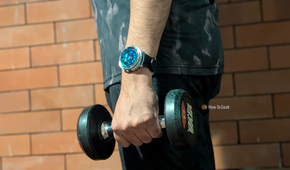 My hand holding a dumb bell in the gym with a dense health data watchface on my Galaxy Watch 8 Classic.