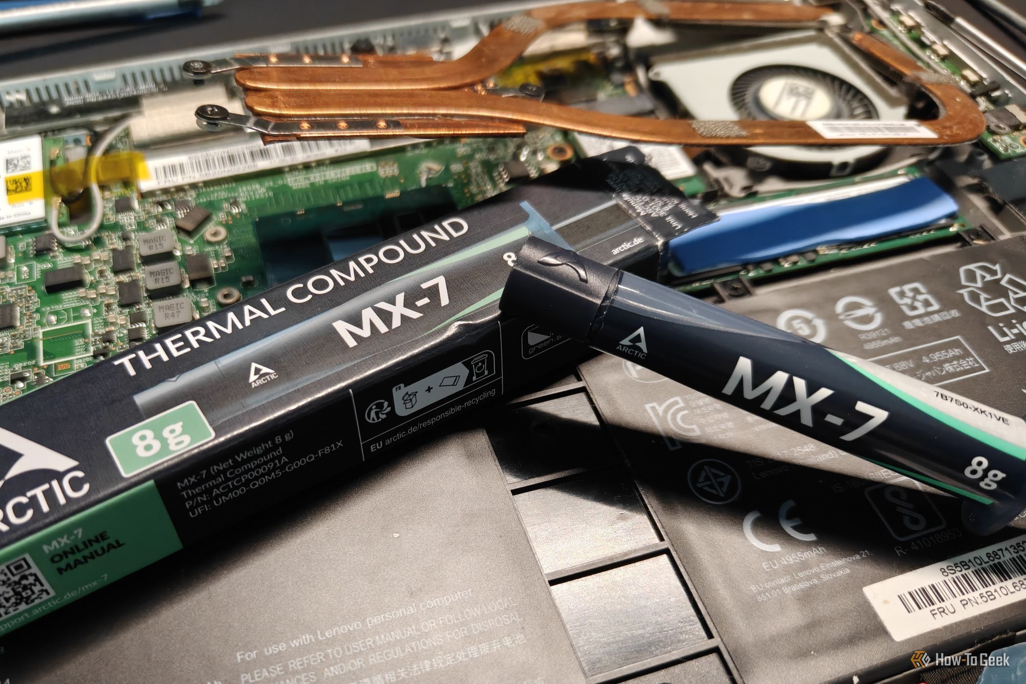 Arctic MX-7 thermal paste next to a disassembled laptop.