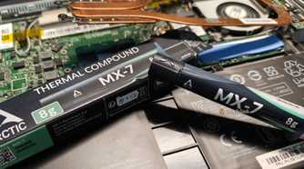 Arctic MX-7 thermal paste next to a disassembled laptop.