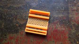 3D printed 100W orange cable clip upside down.