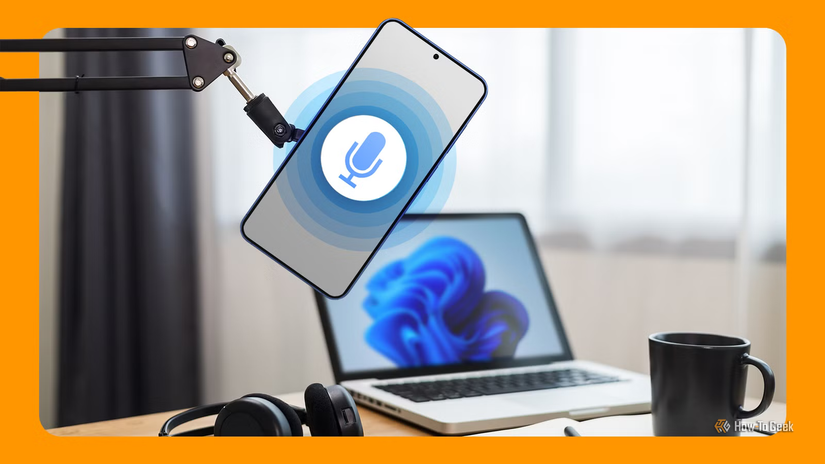 A smartphone with a microphone icon in a microphone arm, with a laptop, headphones, and a coffee mug on a desk in the background.