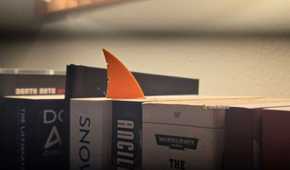 Orange shark-fin bookmark protruding from between science-fiction books on a shelf.