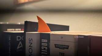 Orange shark-fin bookmark protruding from between science-fiction books on a shelf.
