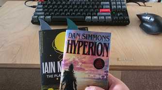 Dan Simmons’ Hyperion held in front of another book, both fitted with shark-fin bookmarks.