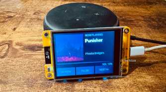 Cheap Yellow Display mounted on an Echo speaker showing a Now Playing screen for Punisher by Phoebe Bridgers with pause and skip controls.