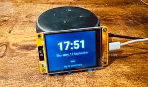Cheap Yellow Display mounted on an Echo speaker showing the time and date with a tap for smart home prompt.