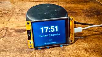 Cheap Yellow Display mounted on an Echo speaker showing the time and date with a tap for smart home prompt.