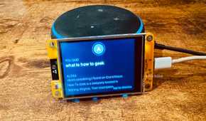 Cheap Yellow Display mounted on an Echo speaker with the blue ring lit showing the spoken command what is how to geek and Alexas response about How To Geek.